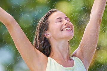 Image showing Woman, rain and freedom with a smile from spring climate, water and weather outdoor in a park. Happy, travel and female person excited on holiday and vacation with hands up from joy in nature