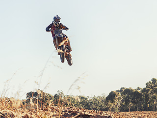 Image showing Motorcycle, person and outdoor for jump in race on trail for competition, air and games on ground. Racer, motorbike and helmet for contest, motor cross and fast transport with flight in countryside