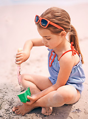 Image showing Little girl, toys and playing with beach sand, castle or summer fun on outdoor holiday or weekend in nature. Female person, child or kid with scoop and shape for building sandcastle by ocean coast