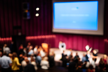 Image showing Blured image of Business and entrepreneurship symposium. Female speaker giving a talk at business meeting. Audience in conference hall. Rear view of unrecognized participant in audience