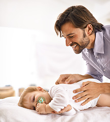 Image showing Father, baby and happiness with play in home for healthy development, parenting and bonding in bedroom. Family, child and man with face, pacifier and comfort for relax, love and care on bed in house
