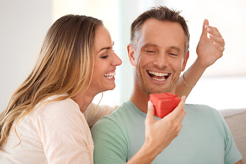 Image showing Woman, surprise or gift for man in lounge, excited or happy couple to celebrate love in home. Wife, care or commitment with present for husband, gratitude or bonding together on sofa on anniversary