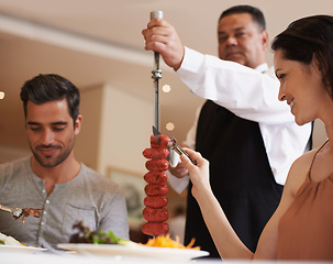 Image showing Couple, waiter and service for lunch in restaurant with meat, happiness and fine dining for anniversary or honeymoon. Man, woman and employee with sausage on skewer, healthy meal and table in London