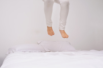 Image showing Jumping, bed and kid with fun, energy and morning in a bedroom with game and feet. Youth, hop and home with a excited child on a duvet in air with crazy play, leap and legs in house with white wall