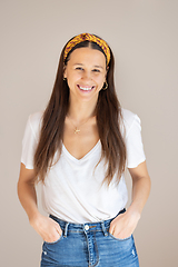 Image showing Portrait of confident beautiful woman with long brown hair, wearing casual clothes, standing in relaxed pose with hands in pockets, smiling with white teeth at camera, studio background.