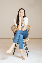 Image showing Portrait of confident beautiful woman with long brown hair, wearing casual clothes, sitting on chair in tight jeans and white t-shirt, studio background