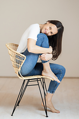 Image showing Portrait of confident beautiful woman with long brown hair, wearing casual clothes, sitting on chair in tight jeans and white t-shirt, studio background