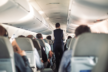 Image showing Interior of airplane with passengers on seats and stewardess in uniform walking the aisle, serving people. Commercial economy flight service concept.