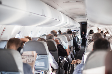 Image showing Interior of airplane with passengers on seats and stewardess in uniform walking the aisle, serving people. Commercial economy flight service concept.