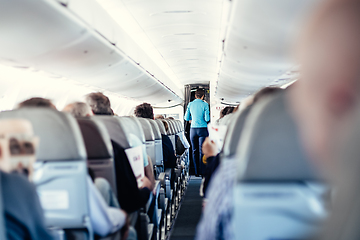 Image showing Interior of airplane with passengers on seats and stewardess in uniform walking the aisle, serving people. Commercial economy flight service concept.