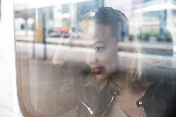 Image showing Woman traveler contemplating outdoor view from window of train. Young lady on commute travel to work sitting in bus or train.