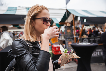 Image showing Beautiful young woman holding delicious organic salmon vegetarian burger and drinking homebrewed IPA beer on open air beer an burger urban street food festival in Ljubljana, Slovenia.