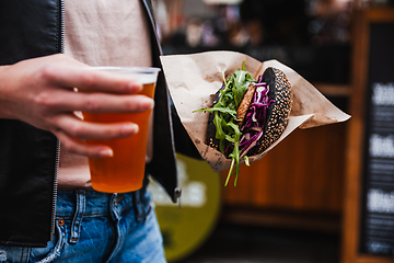 Image showing Close up of woman hands holding delicious organic salmon vegetarian burger and homebrewed IPA beer on open air beer an burger urban street food festival in Ljubljana, Slovenia.