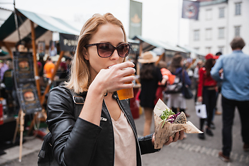 Image showing Beautiful young woman holding delicious organic salmon vegetarian burger and drinking homebrewed IPA beer on open air beer an burger urban street food festival in Ljubljana, Slovenia.