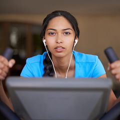 Image showing Woman, earphones and cycling in portrait, bike and stationary machine for workout at club. Female person, cardio and podcast or sound and audio, playlist and equipment for fitness and body health