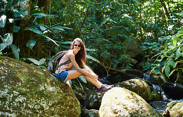 Image showing Woman, hiking and river in tropical rainforest with smile for adventure, journey and rocks with backpack. Girl, outdoor and bag by water, earth and trees in jungle on holiday with freedom in Colombia