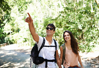 Image showing Happy couple, backpack and pointing with direction in forest for hiking, adventure or outdoor journey in nature. Young man and woman holding hands with bag for trekking, sightseeing or destination