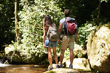 Image showing Couple, back and rocks for hiking by river, environment and memory on holiday with holding hands. Man, woman and bag for trekking, direction or search in rainforest with water at location in Colombia