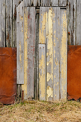 Image showing Weathered wooden door with peeling yellow paint on a rustic barn