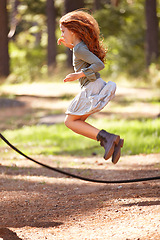 Image showing Jump, rope and girl outdoor for game in forest, park or playing on summer, holiday and vacation. Child, skipping and energy for fun activity in nature with trees in backyard or garden with kid in air