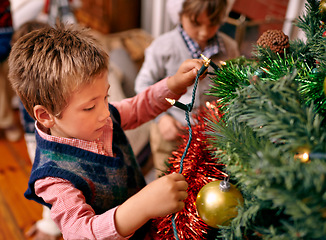 Image showing Little boy, decorating and tree for Christmas with ornaments, lights and celebration for season in season. Child, working and love for festive tradition in family home, kids and enjoying holiday