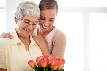 Image showing Senior woman, daughter and hug with flowers, present and care for love, bonding or reunion at family home. People, elderly mom and mothers day celebration for connection, gift or bouquet in apartment