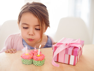 Image showing Cupcakes, blowing candles and girl with birthday, kid and gift with happiness, candy and home. Childhood, celebration and excited with dessert or present with party or box with wow, sweet or surprise