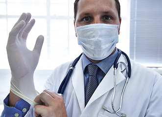 Image showing Portrait, doctor and man put on gloves in mask for protection or safety in hospital. Face, medical professional and ppe to prepare for surgery, treatment or prevention of disease in healthcare clinic