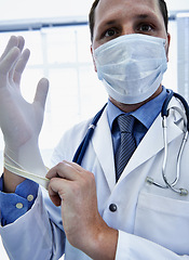 Image showing Portrait, doctor and man putting on gloves for safety or protection in hospital. Face mask, medical professional or ppe to prepare for surgery, treatment or prevention of disease in healthcare clinic