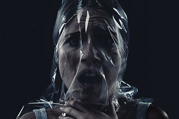 Image showing Scary, face and woman with plastic or bag in horror, drama or death in dark background of studio. Suffocating, murder and girl with fear from crime, victim and trapped in trash, garbage or pollution
