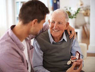 Image showing Father, adult son and medal for gift, support and congratulations with celebration and bonding at home. Men in living room, family time with reward or award for present, happiness and gratitude