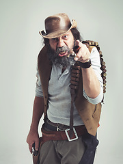 Image showing Senior cowboy, point and angry face at studio, costume and holster for western portrait looking scruffy. Old man, sheriff hat and dirty male for texas, grey background and annoyed gesture for outlaw