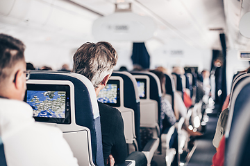 Image showing Interior of airplane with passengers on seats and stewardess in uniform walking the aisle, serving people. Commercial economy flight service concept.