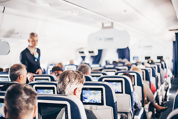 Image showing Interior of airplane with passengers on seats and stewardess in uniform walking the aisle, serving people. Commercial economy flight service concept.