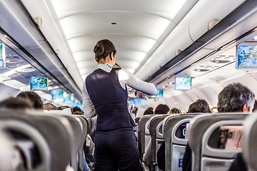 Image showing Interior of airplane with passengers on seats and stewardess in uniform walking the aisle, serving people. Commercial economy flight service concept.