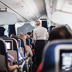 Image showing Interior of airplane with passengers on seats and stewardess in uniform walking the aisle, serving people. Commercial economy flight service concept.