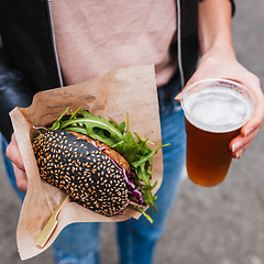 Image showing Close up of woman hands holding delicious organic salmon vegetarian burger and homebrewed IPA beer on open air beer an burger urban street food festival in Ljubljana, Slovenia.