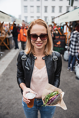 Image showing Beautiful young woman holding delicious organic salmon vegetarian burger and homebrewed IPA beer on open air beer an burger urban street food festival in Ljubljana, Slovenia.