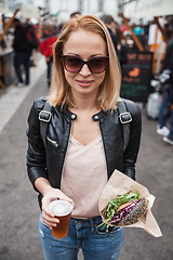 Image showing Beautiful young woman holding delicious organic salmon vegetarian burger and homebrewed IPA beer on open air beer an burger urban street food festival in Ljubljana, Slovenia.