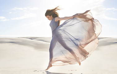Image showing Desert, woman and fashion with dress, jumping and relaxing with confidence and getaway trip. Person, outdoor and sand with girl and clouds with fabric, fun and summer with weekend break and active
