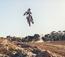 Image showing Person, jump and motorbike of professional motorcyclist in the air for trick, stunt or race on outdoor dirt track. Expert rider on bike or scrambler in dunes or extreme sport with blue sky background
