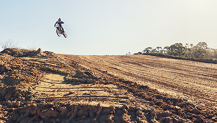 Image showing Person, jump and dirt track of professional motorcyclist in the air for trick, stunt or race on outdoor terrain. Expert rider on motorbike or scrambler for extreme sports with blue sky background