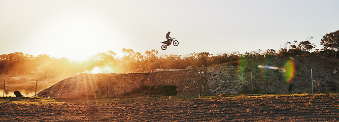 Image showing Person, jump and professional motorcyclist on banner in the air for trick, stunt or ramp on outdoor dirt track. Expert rider on motorbike with lift for extreme sports or rally challenge in the sunset