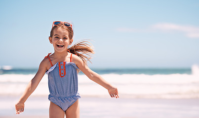 Image showing Happy, portrait and little girl playing at the beach for fun holiday, weekend or outdoor summer. Excited female person, child or young kid with smile in happiness for day by the ocean coast in nature