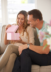 Image showing Woman, surprise or open gift of man in lounge, excited or happy couple to celebrate love in home. Husband, care and guessing with present for wife, gratitude and bonding on sofa for valentines day