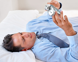 Image showing Businessman, alarm clock and upset to wake up for work and schedule in the bed at home. Mature male person, clock and frustrated with watch for appointment and sleep or fatigue while lying in bedroom