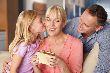 Image showing Family, mothers day gift and kiss on sofa in living room of home for love, celebration or surprise. Birthday, box or present with mom, dad and girl in apartment together for affection or excitement