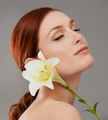 Image showing Face, skincare and woman with flower, lily and natural beauty isolated on a gray studio background. Floral cosmetics, organic and model with eyes closed for glow, wellness or healthy skin with makeup