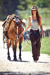 Image showing Woman, portrait and cowgirl walking with horse in countryside for ride, journey or outdoor adventure in nature. Female person or western rider with hat, saddle and animal stallion at ranch or farm