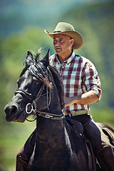 Image showing Cowboy, nature and man riding horse with saddle on field in countryside for equestrian or training. Western, summer and rodeo with mature horseback rider on animal at ranch outdoor in rural Texas